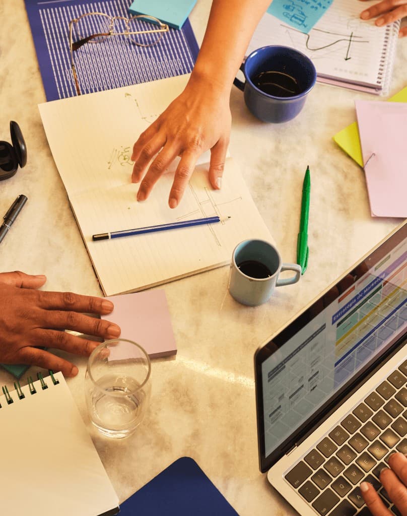 People working together around a table with notebooks, sticky notes and a laptop